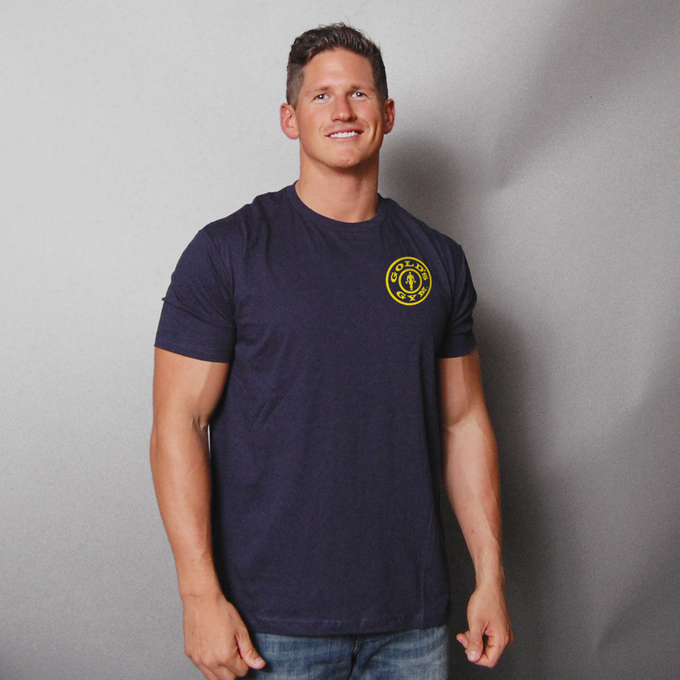 photo of model wearing basic left chest tee in navy. golds gym weight plate logo in yellow on upper left chest. 