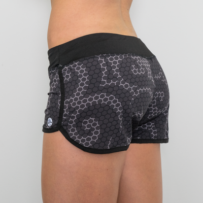 back view photo of model wearing advance ladies woven short in steel geo hex. waistband in black. golds gym weight plate logo in white. black overlapped seam on sides and around legs.