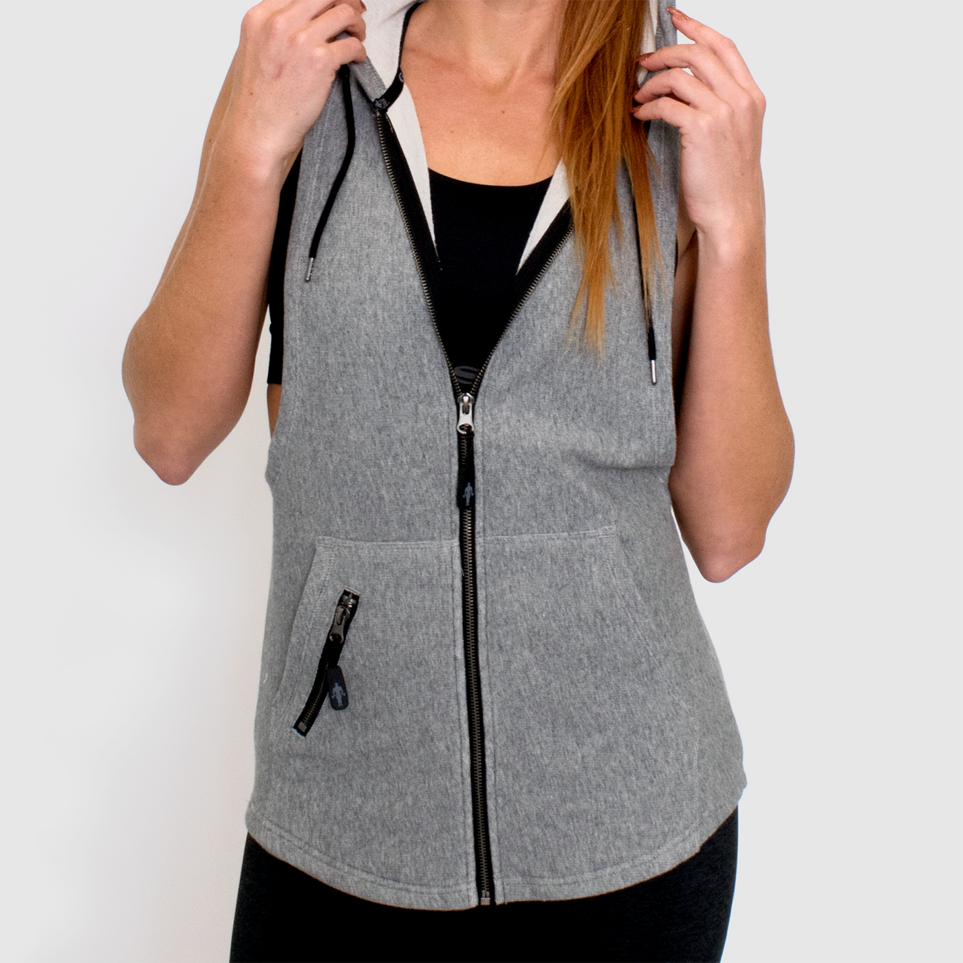 detail photo of model advance ladies sleeveless hoodie in grey. two front pocket seperated by a zipper. front zipper pocket on outside of right side pocket. muscle joe logo for zipper pulls.