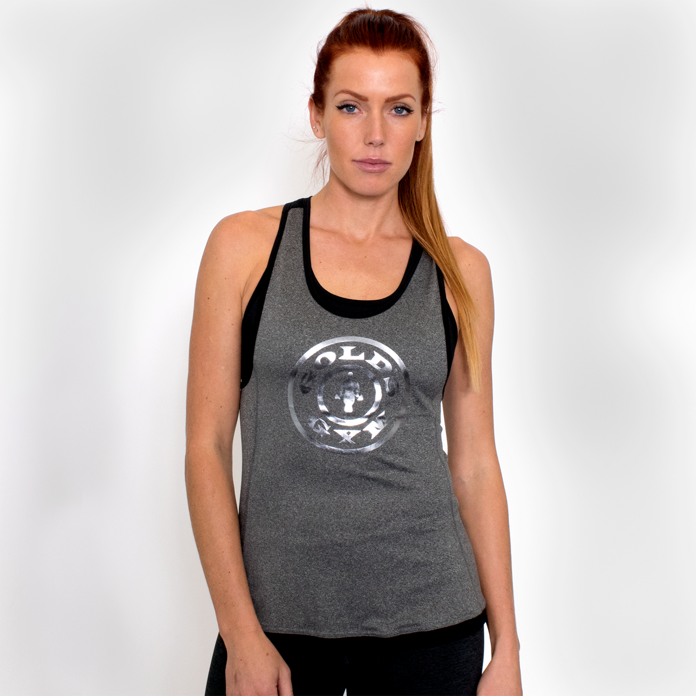 photo of model wearing ladies foil stringer in grey/black. golds gym weight plate logo in reflective silver on front.