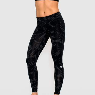 photo of model wearing advance ladies legging in steel geo hex. golds gym weight plate logo printed below left knee in white.