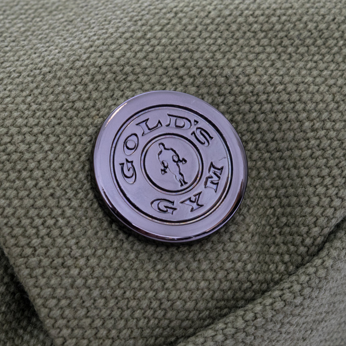 detail photo of golds gym weight plate logo metal accent on washed olive waist pack