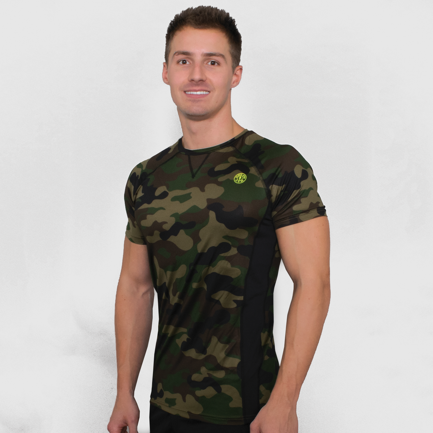 photo of model wearing advance performance raglan crew in green camo. golds gym weight plate logo in yellow top left shoulder. black seam visible from neck line to armpit. v stitch bleow neckline in center. black stripes on both sides under arms