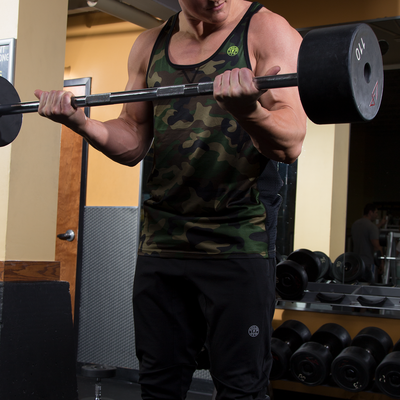 photo of model lifting barbell wearing advance performance stringer in green camo. golds gym weight plate logo in yellow on upper left chest. black trim around arm and neck holes. black stripes on sides. stitched v under neck line. 