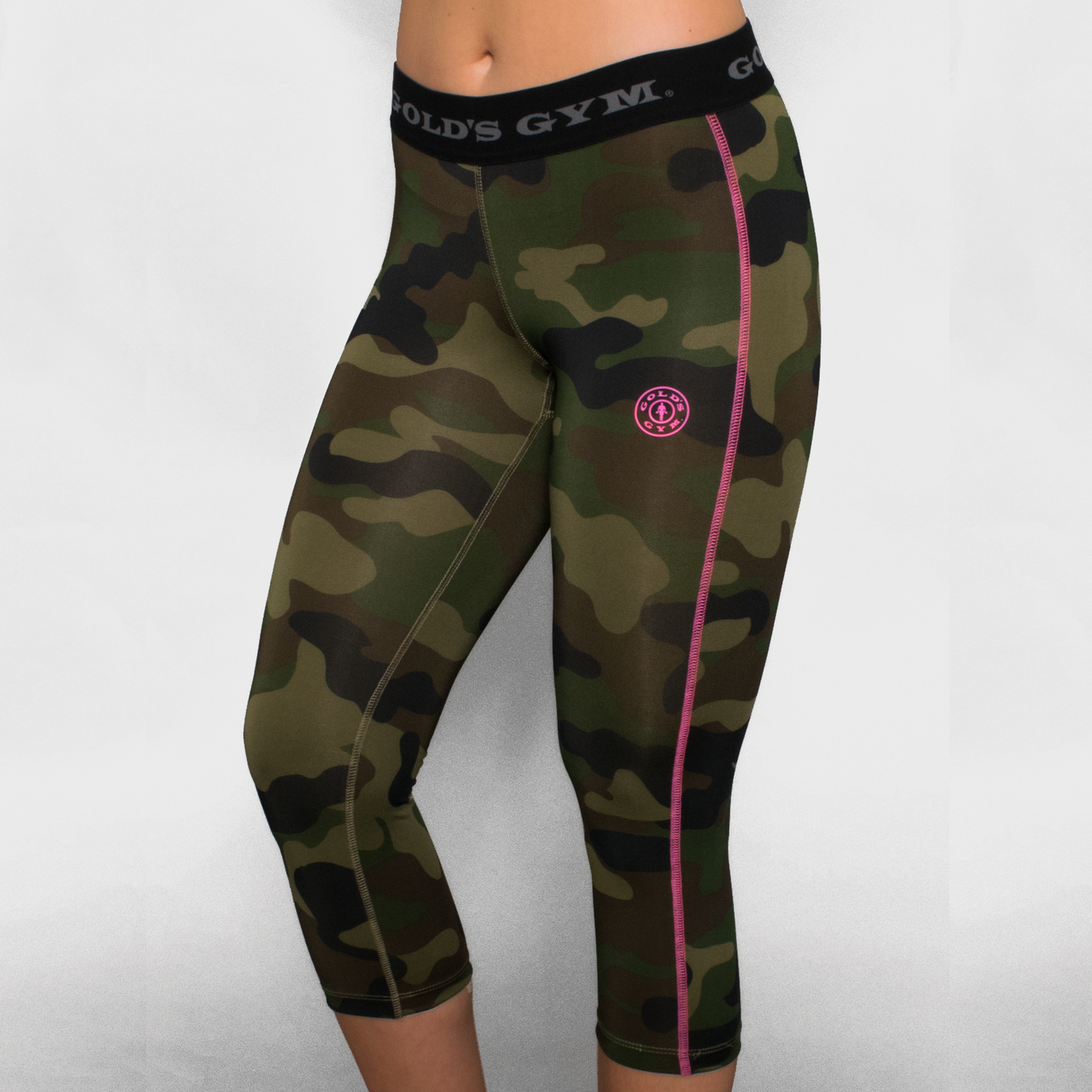 photo of model wearing advance 3/4 performance tights in green camo. golds gym printed on waistband. golds weight plate logo in pink on left leg. pink seam on outside of left leg.